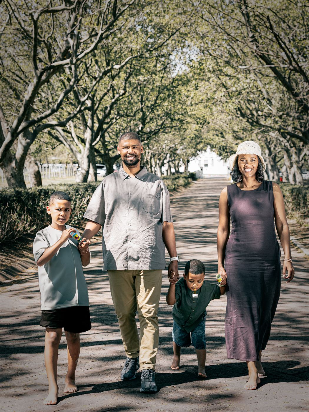 Family of four walking barefoot down a tree-lined avenue