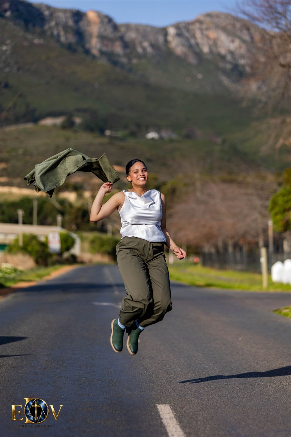 Young woman caught mid-jump on a mountain road, jacket in hand