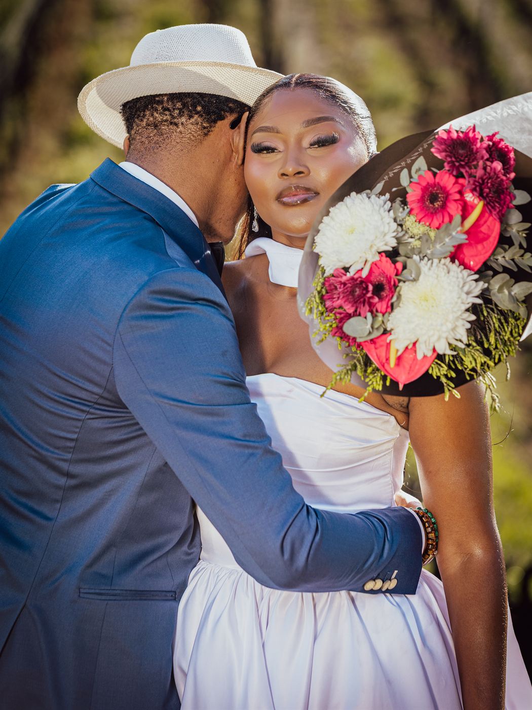 Bride looking straight to camera as her partner leans in, a bright bouquet beside her